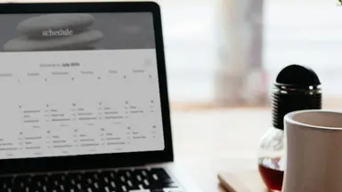 schedule on laptop on a desk with coffee and flowers