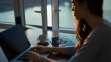woman with brown sitting at desk with laptop 