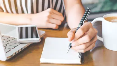 woman in striped shirt sitting at desk writing in notebook