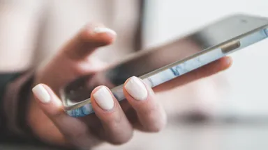 woman with light pink manicure holding smartphone