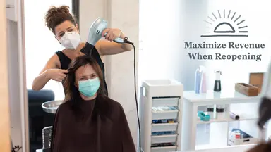 A hair stylist wears a mask while she blow dries a client's hair