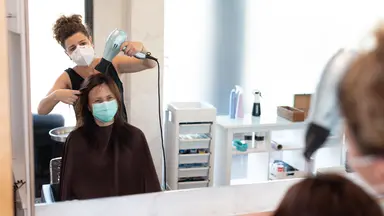 Hair stylist wearing a mask while blow drying hair