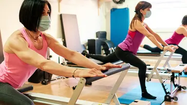 three women in masks on pilates reformers
