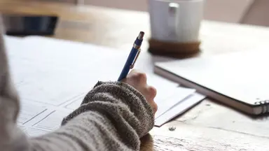 woman in sweater writing at desk with pen