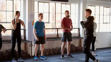 Man speaks to a group of five people in fitness studio.