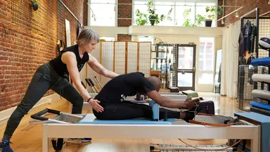 woman helping man on pilates reformer machine in studio