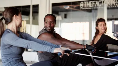 two women and one man on rowing machine at gym