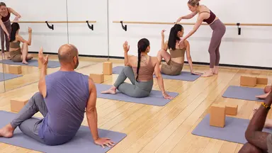 yoga class full of people and one instructor providing adjustments