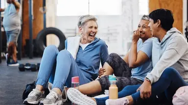 Three women in blue shirts sitting and laughing after a workout class