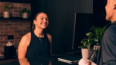 A client and staff member at the front desk of a fitness business.
