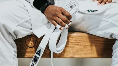 A person dressed in martial arts attire sits on a bench holding their white belt.