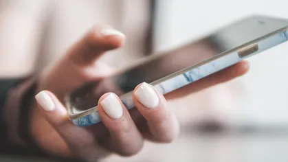 woman with light pink manicure holding smartphone