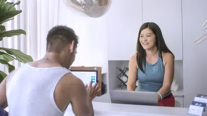 Client being greeted by staff and self-checking in at the front desk of a fitness studio using an iPad
