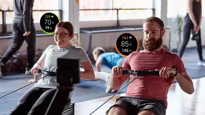 Two people using rowing equipment with FitMetrix data display above