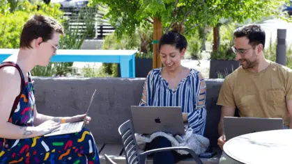 A group of people sitting outside with laptops, collaborating