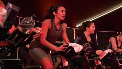 Group fitness class of many people on excercise bikes in room that is lit by red lights