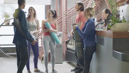 People with yoga mats smiling at front desk