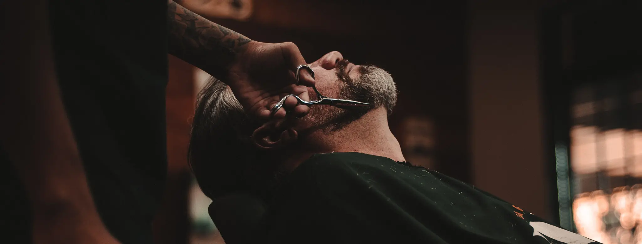 Man reclined in chair and getting beard his trimmed in barbershop