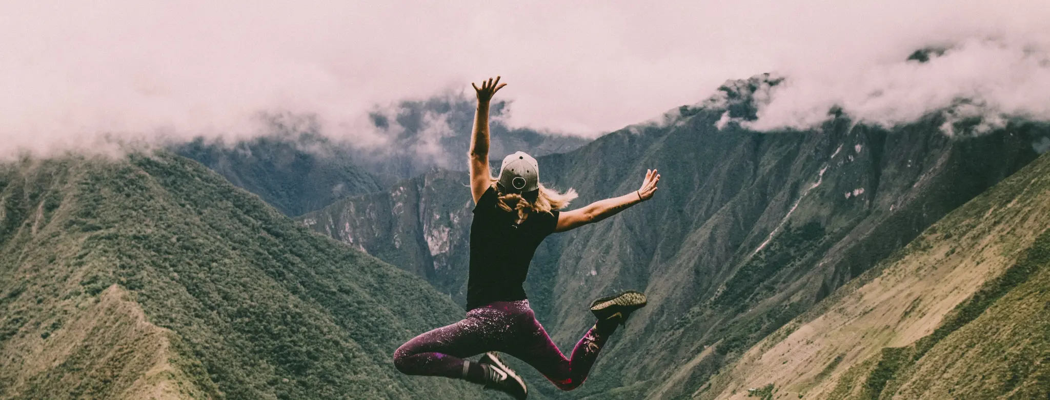 Woman jumping for joy in front of clouds and mountains