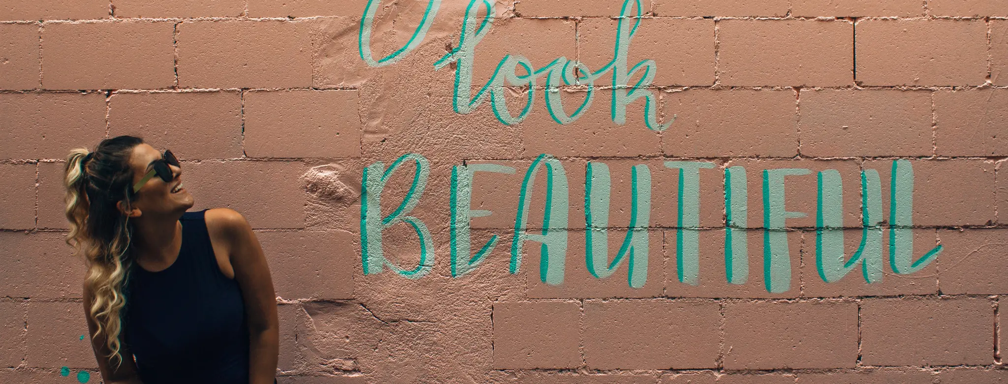 Woman leaning on a painted brick wall with a "You look beautiful" mural