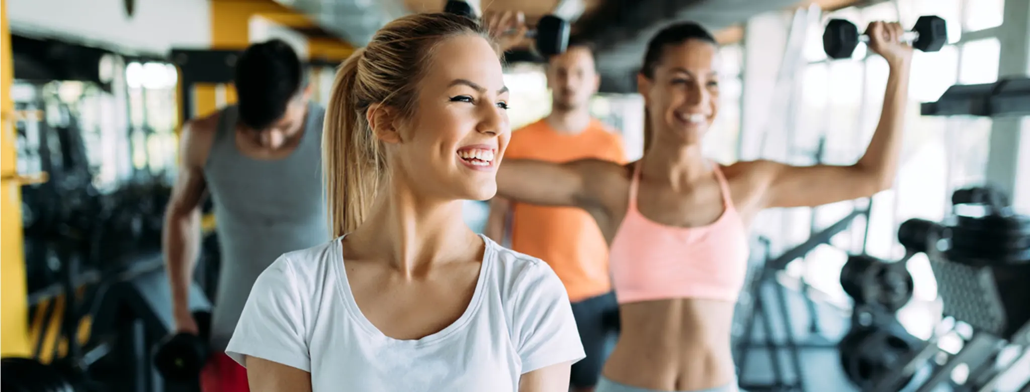 blonde woman lifting weights with others in gym