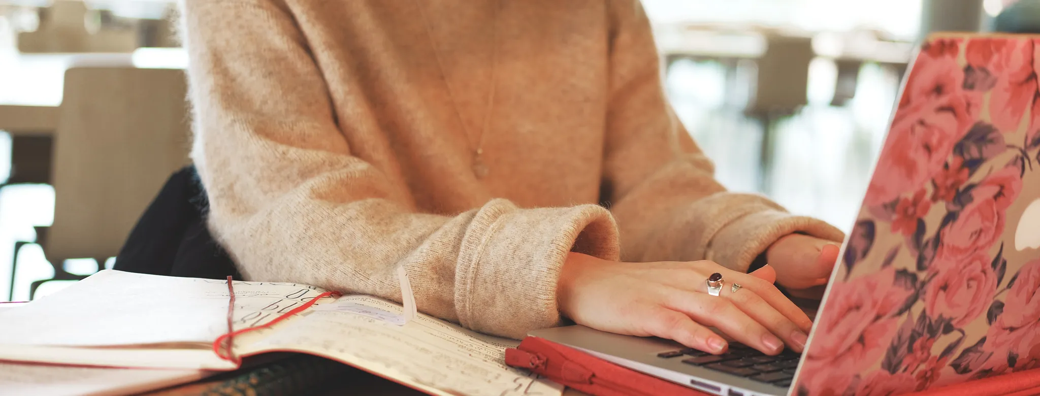 woman in tan sweater with a pink floral laptop