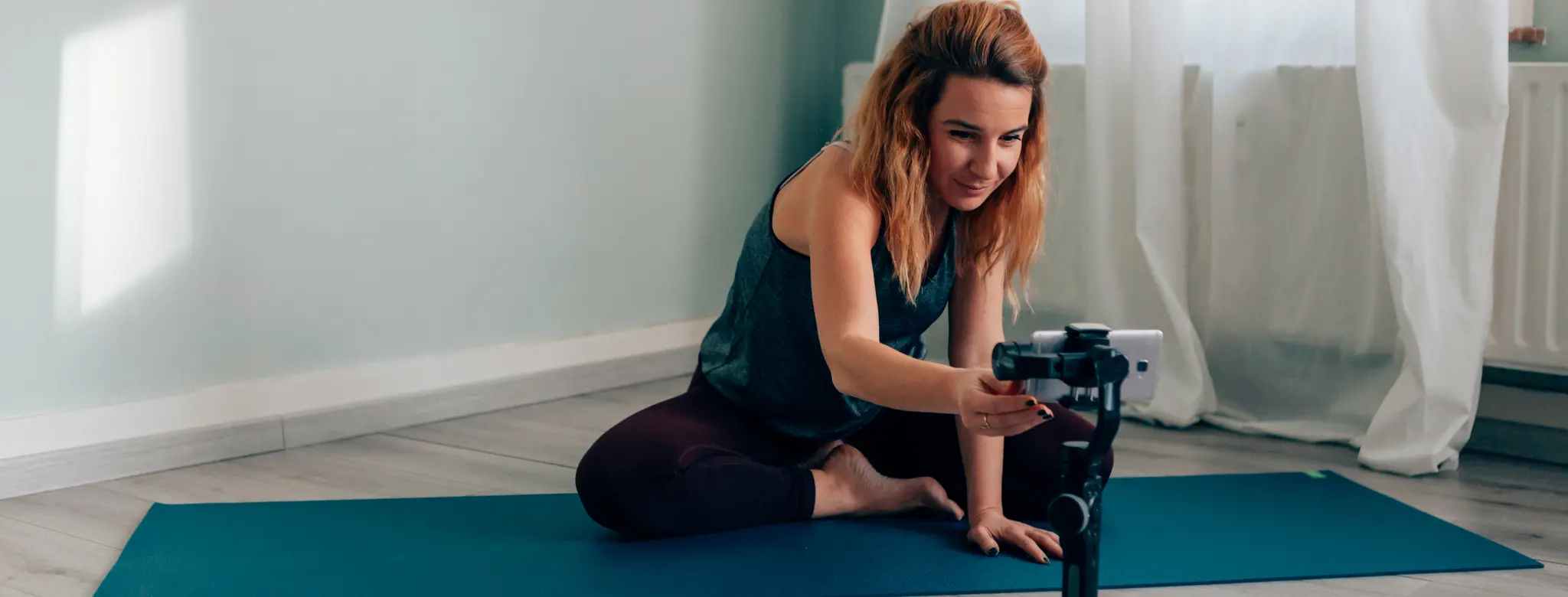 Fitness instructor at home on a mat and setting up virtual class with a phone on a tripod