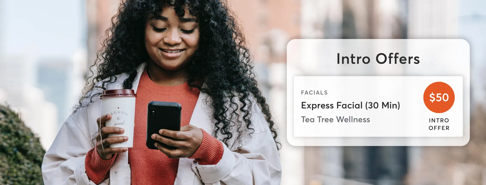 woman walking with coffee on smartphone booking fitness class