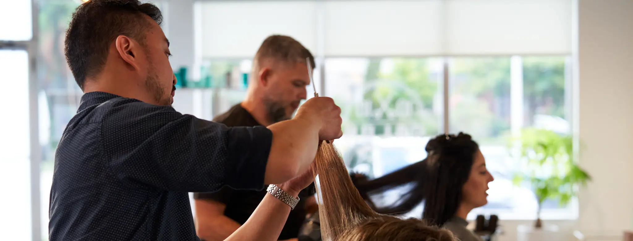 two women getting haircuts in salon by male hair stylists