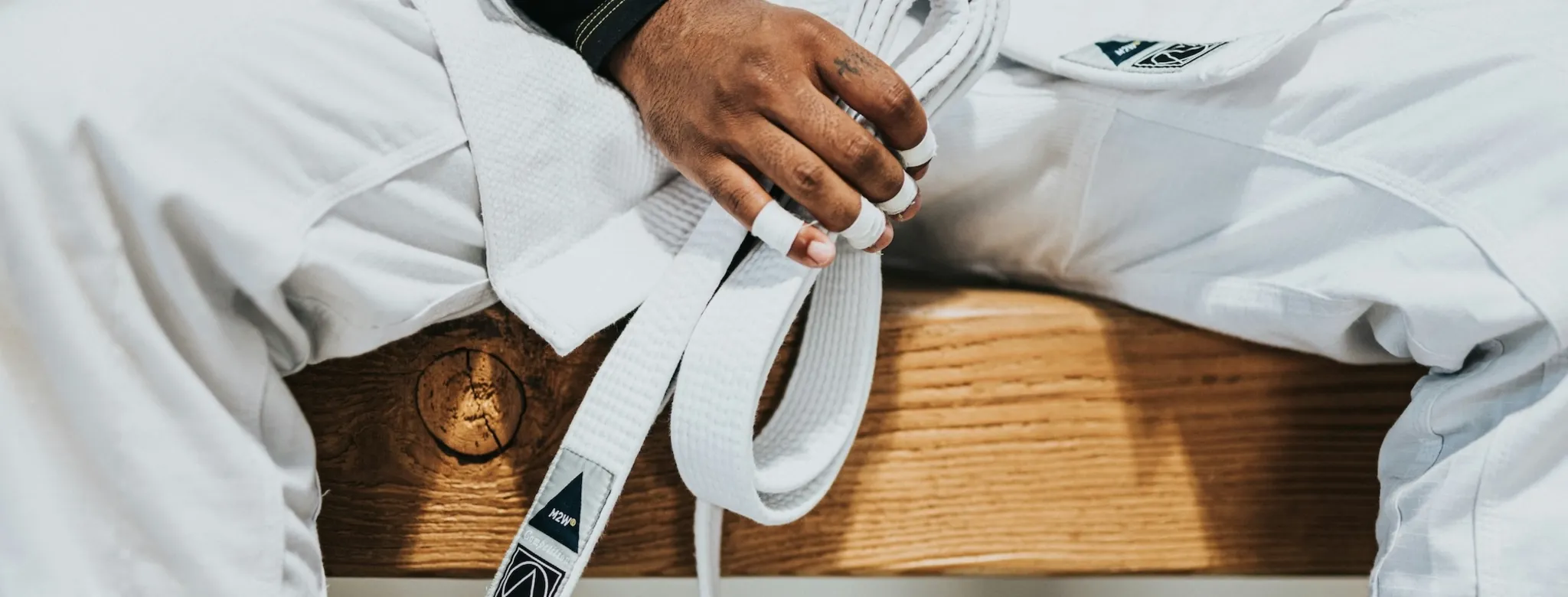A person dressed in martial arts attire sits on a bench holding their white belt.
