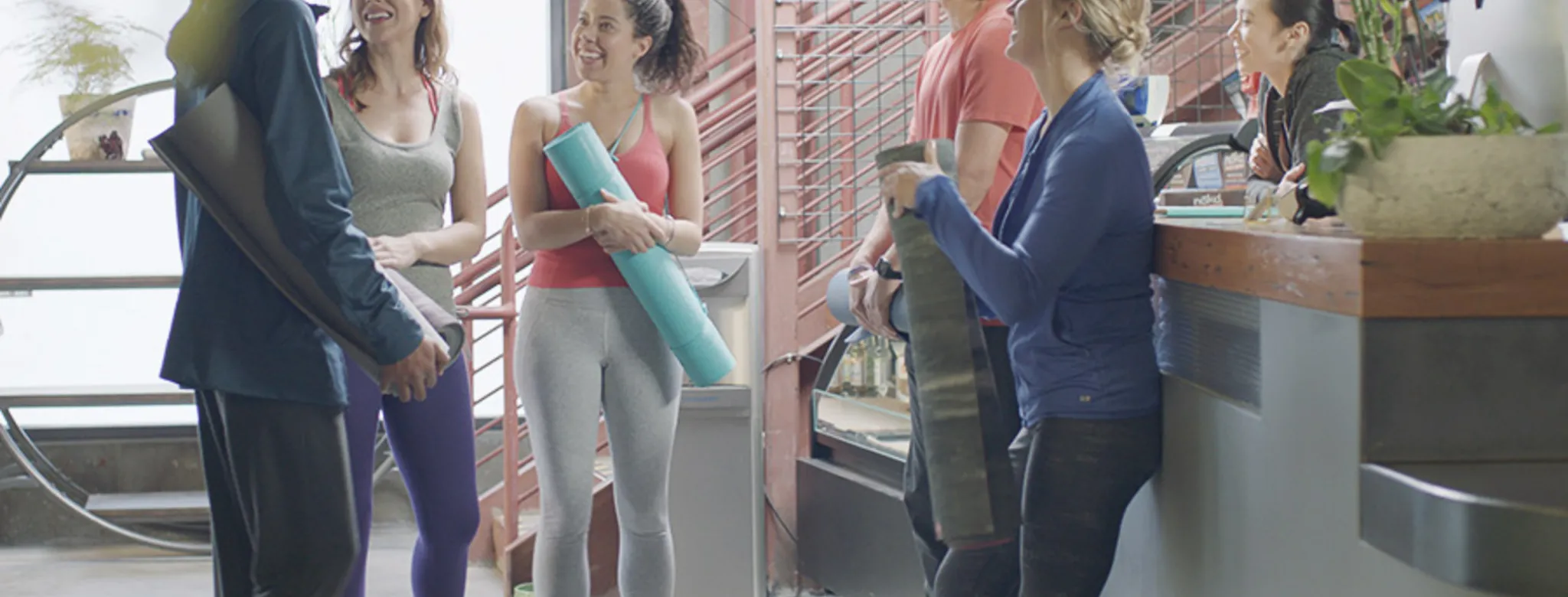 People with yoga mats smiling at front desk