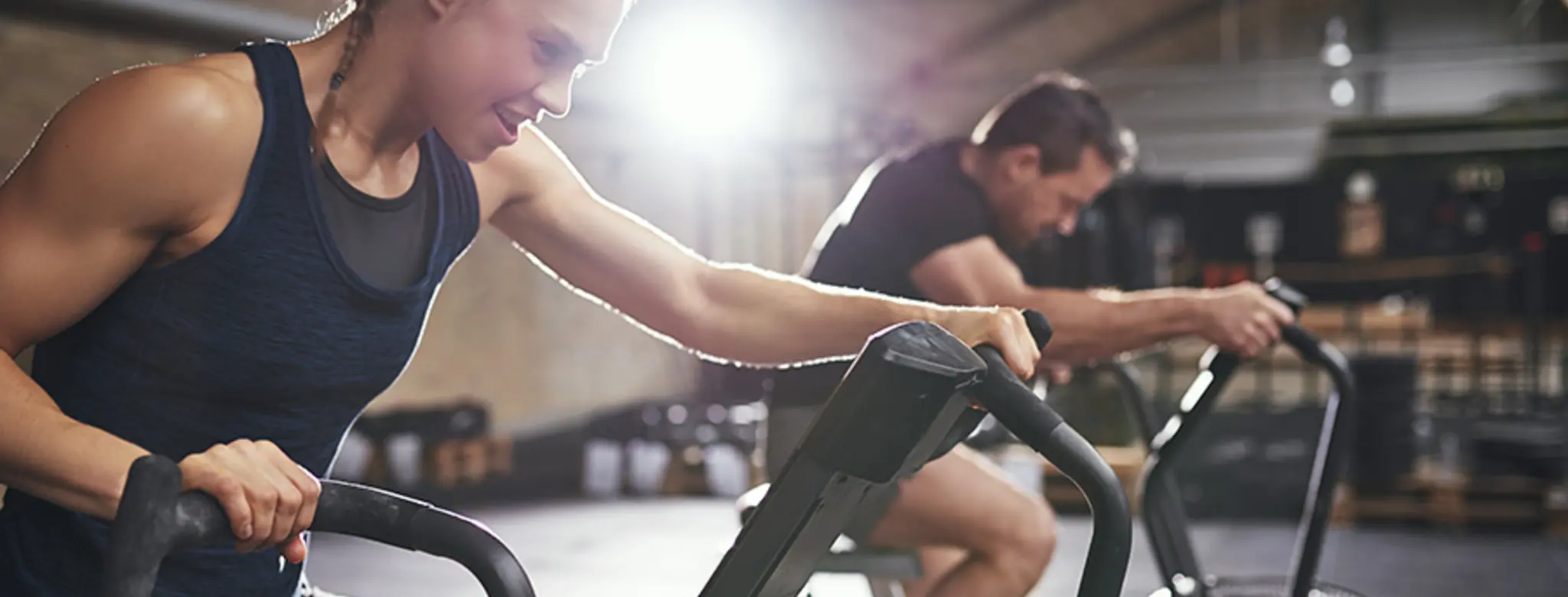 Woman working hard on stationary bike, man biking in background after purchasing introductory offers