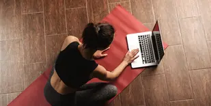 Woman sitting on a yoga mat on her laptop