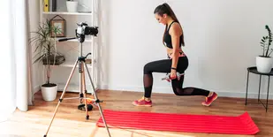 Fitness instructor filming a video workout at home in front of a camera on a tripod
